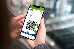März Zwei Hände halten ein Smartphone, dessen Bildschirm einen QR-Code anzeigt