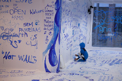 Ein Kind malt mit einem Pinsel und blauer Farbe an die Wand