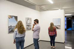 UmBAUkultur Drei Personen schauen sich Fotografien an, die an einer weißen Wand hängen.