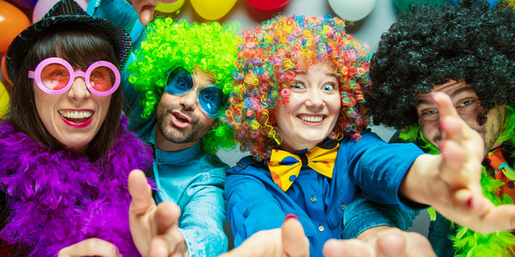 Karneval Vier bunt kostümierte Personen, im Hintergrund sind Luftballons zu sehen