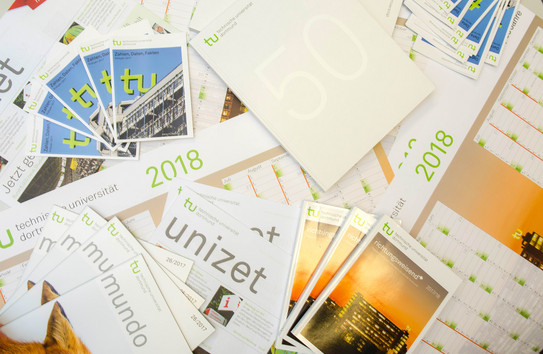 Presse Verschiedene Publikationen wie die Unizet, die Mundo, Infobroschüren und die Festschrift zum 50-Jährigen Jubiläum liegen verstreut auf einem Holztisch