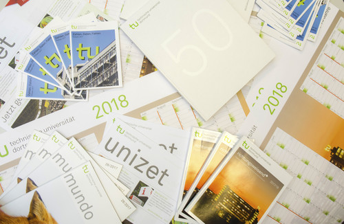 Verschiedene Publikationen wie die Unizet, die Mundo, Infobroschüren und die Festschrift zum 50-Jährigen Jubiläum liegen verstreut auf einem Holztisch