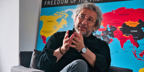 Can Dündar Can Dündar sitzt auf einem Sessel. Im Hintergrund eine Weltkarte.