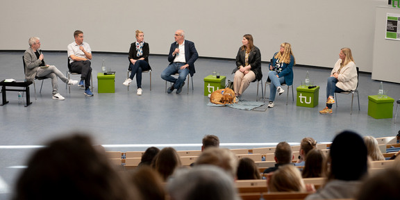 Mehrere Personen sitzen vorne im Audimax in einer Gesprächsrunde zusammen.
