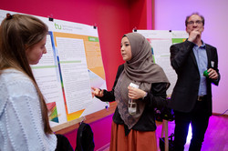 A woman is explaining something to another woman. They stand in front of a standing wall