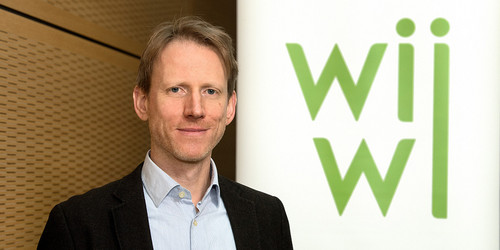 Ein Portraitfoto von Michael J. Böhm neben dem grünen Schriftzug der "wiwi"-Fakultät.