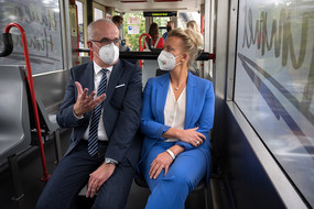 Prof. Manfred Bayer und Ina Brandes sitzen Nebeneinander in der H-Bahn, die über den Campus der TU Dortmund fährt.