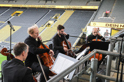 Four cellists play in front of a filled grandstand in the stadium.