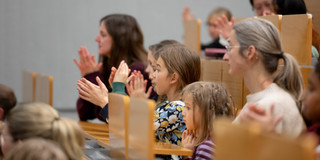 Kinder und ihre Familien sitzen in einem Hörsaal und klatschen Beifall.