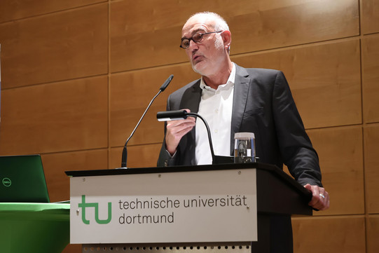 A man with glasses stands at a lectern and speaks.