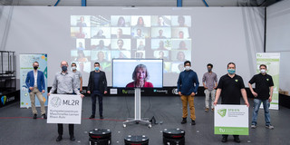 Hackathon Gruppenbild mit mehreren Personen, im Hintergrund eine Leinwand mit Teilnehmern von Videochats