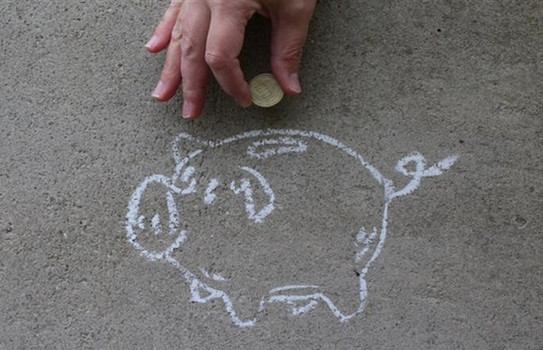 Ein auf dem Boden mit Kreide aufgemaltes Sparschwein Eine Hand wirft eine Münze in ein mit Kreide aufgemaltes Sparschwein