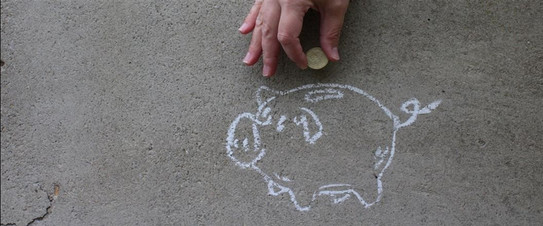 Eine Hand wirft eine Münze in ein mit Kreide aufgemaltes Sparschwein