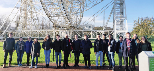 Eine Gruppe junger Menschen posieren für ein Gruppenfoto vor einem Gebilde aus weißem Metall.