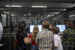 Eine Gruppe von jungen Leuten steht vor zwei Computerbildschirmen.