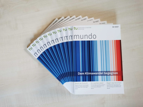 Several issues of mundo 32 with the overriding theme "Confronting Climate Change" lie fanned out on a wooden table.