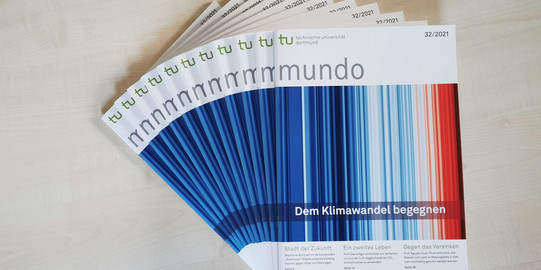 Several issues of mundo 32 with the overriding theme "Confronting Climate Change" lie fanned out on a wooden table.
