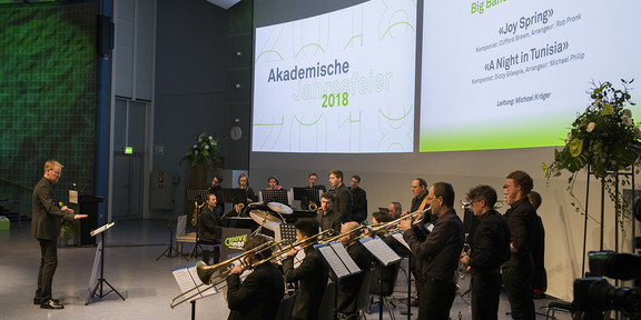 Akademische Jahresfeier_5 Band spielt auf der Bühne, auf der Leinwand im Hintergrund steht "Akademische Jahresfeier 2018"