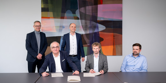 Gruppenfoto mit fünf Personen, von denen zwei ein Papier unterschreiben