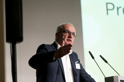 A man in a suit stands at a lectern.