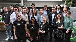 April Eine große Gruppe Menschen, einige davon halten gläserne Pokale in den Händen