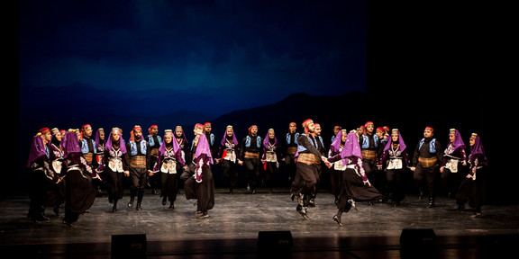 Viele Tänzer*innen stehen auf einer Bühne, sie tragen traditionelle anatolische Kostüme