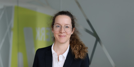 Portrait photo of Prof. Almut Balleer in front of a gray and yellow blurred background