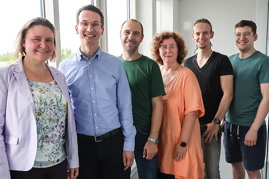 Vier Männer und zwei Frauen stehen leicht versetzt nebeneinander und posieren für ein Foto.