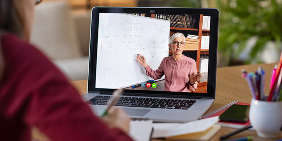 Girl sits at a desk and watches an educational video where a woman is explaining something on a blackboard.