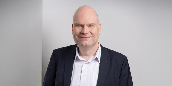 Porträtfoto von Dr. Jan-Martin Wiarda auf hellgrauem Hintergrund. Dr. Wiarda trägt einen dunklen Anzug und lächelt in die Kamera.