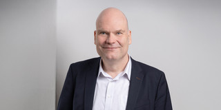 Porträtfoto von Dr. Jan-Martin Wiarda auf hellgrauem Hintergrund. Dr. Wiarda trägt einen dunklen Anzug und lächelt in die Kamera.