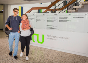  A student couple walks past a TU logo in the foyer of a building.
