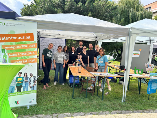 Mehrere Personen stehen unter einem Pavillon auf einer Wiese und präsentieren einen Informationsstand der TU Dortmund. Auf einem Banner ist „Talentscouting“ zu lesen, daneben liegen Flyer und Materialien auf den Tischen – die Szene zeigt das Sommerfest der TU Dortmund im Jahr 2025.
