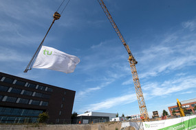 An einem Baukran weht eine TU-Dortmund-Fahne über einer Baugrube.