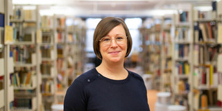 Foto: Eine Person steht im Gang einer Bibliothek zwischen Bücherregalen.