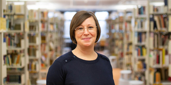 Foto: Eine Person steht im Gang einer Bibliothek zwischen Bücherregalen.