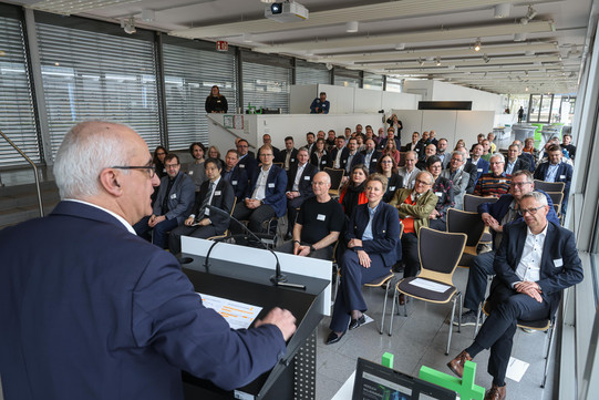 Foto: Eine Person spricht an einem Rednerpult vor einem sitzenden Publikum.