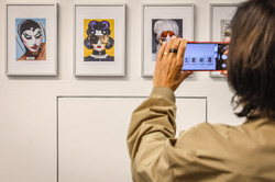 Photo: A woman with dark hair is taking pictures of the art exhibition with her cell phone.