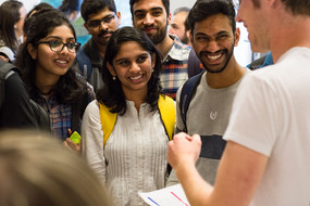 A young man in a white T-Shirt explaining something to a group of international students