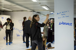 Eine Frau bemalt die Wand. Im Hintergrund stehen Personen