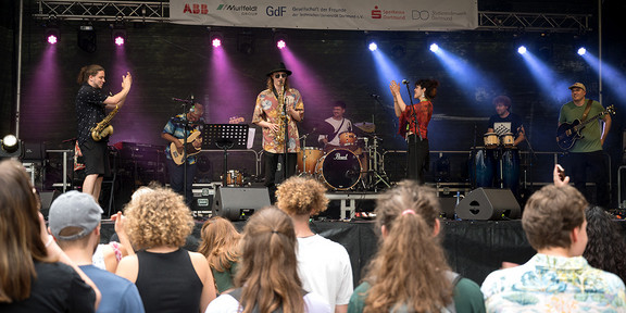 Publikum steht vor einer Bühne, auf der Musik gespielt wird