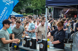 Ein Essenstand auf dem Sommerfest. Im Hintergrund eine große Menge an Menschen und eine Bühne.