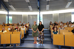 Eröffnungsveranstaltung Zwei Frauen stehen vor den Rängen des Hörsaals, im Hintergrund sind Teilnehmende.