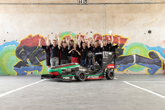 GET racing bei Formula Student France Gruppenfoto des GET racing Teams mit Rennwagen vor einer Mauer mit Graffiti. Die Studierenden jubeln und heben die Arme in die Höhe.