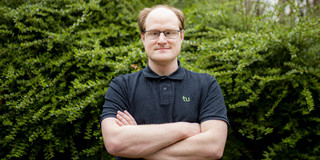 Daniel Horn from the Faculty of Statistics in front of green bushes