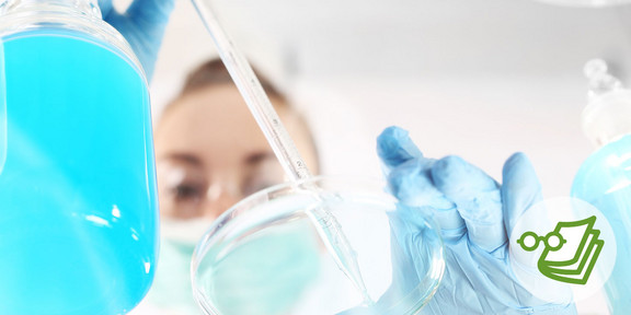 Eine Person mit Mundschutz gibt über eine Pipette eine Flüssigkeit in eine Petrischale.