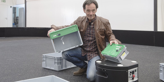Sondhof-Logistik Ein Mann kniet am Boden und hält Plastikkisten in den Händen.