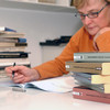 A senior citizen learns surrounded by stacks of books at a table