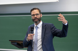 A man in a suit gives a speech with a microphone in his hand.