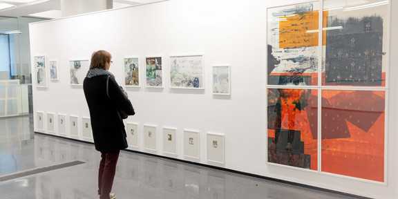 Eine Frau steht in einer Ausstellung und betrachtet Bilder, die an einer Wand hängen.